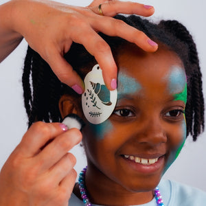 Step one, Dabbing sparkle turquoise on both sides of the face with a sponge, then painting a seahorse shape with bright green on one side, filling it in, adding ochre yellow to the belly, and bright pink to the mane.