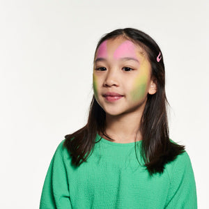 Step one, showing the start of creating semi-circles using pink over both eyebrows, yellow on both cheeks and green on lower face.